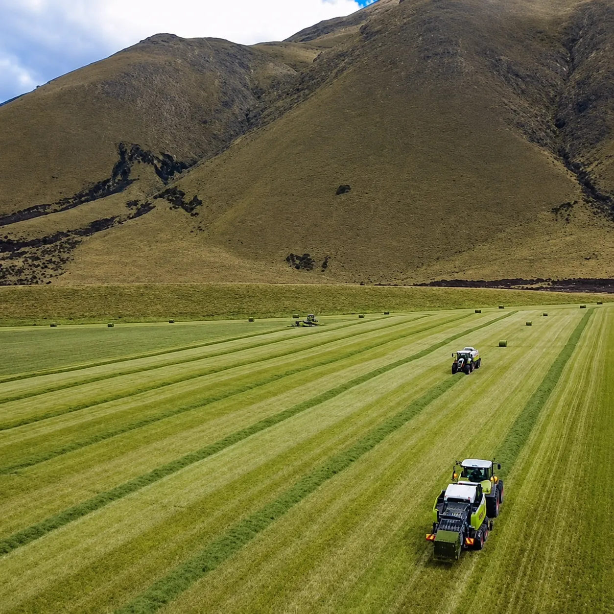 Tractors rowing up a green paddock below the hills